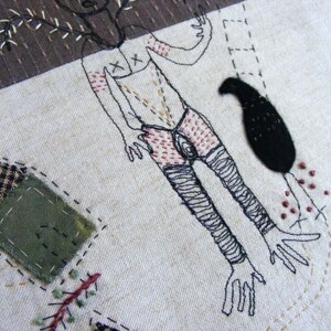 May include: Embroidered artwork featuring a stylized human figure with a tree growing from its head, a black bird, and a black circle. The artwork is stitched on a beige fabric background.