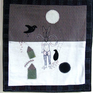 May include: A black and white embroidered wall hanging with a stylized figure, two birds, and geometric shapes. The background is a dark gray fabric with a white moon.