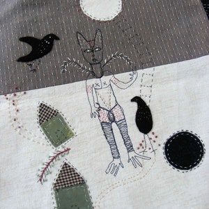 May include: A white fabric background with black and white embroidered figures. A black bird with a long tail is flying above a figure with a long neck and long legs. The figure has a white body with black lines and a black circle on its chest. The figure is standing next to a ladder with a black bird on the top rung. There are two small houses with black and white checkered roofs and green walls. The background is a dark gray fabric with a white circle in the upper left corner.