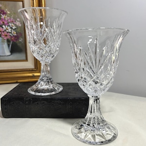 May include: Two clear crystal wine glasses with intricate diamond and vertical cut patterns. The glasses have a tulip-shaped bowl and sit on a decorative stem and base. The glasses are displayed on a dark surface.