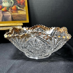 May include: A clear, cut-glass bowl with a scalloped rim and gold trim. The bowl features a starburst pattern in the center and a decorative design around the sides. The bowl is likely vintage and suitable for serving.