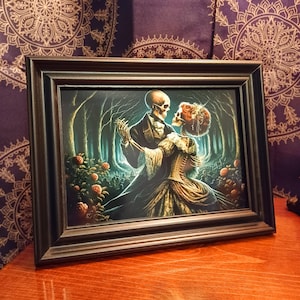 May include: A framed print of a skeletal couple dancing in a dark forest setting. The woman is wearing a long, flowing gown with a corset, and the man is wearing a suit. The print is surrounded by a dark wood frame.