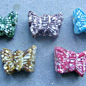 May include: Five ceramic butterfly beads with white speckles on a blue, green, brown, purple, and red background.