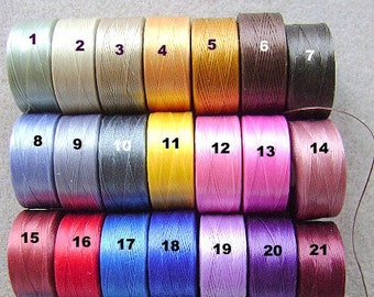 May include: A collection of twenty-seven spools of thread arranged in a grid, each labeled with a black number from 1 to 27. The spools feature a wide variety of colors including shades of beige, brown, yellow, pink, red, blue, purple, and green.