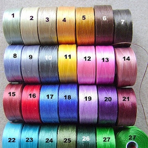 May include: Twenty-seven spools of thread in various colors, numbered 1 through 27. The spools are arranged in three rows of nine spools each.