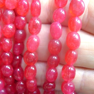 May include: A strand of bright red oval-shaped beads. The beads are smooth and glossy, and they are strung on a clear thread.
