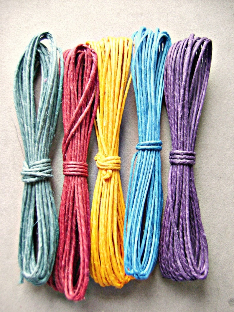 Puede incluir: Cinco manojos de cordel trenzado dispuestos verticalmente en fila. Los colores de izquierda a derecha son verde apagado, rojo intenso, amarillo brillante, azul cielo y violeta vibrante. Cada manojo est&aacute; sujeto en el centro con un lazo.