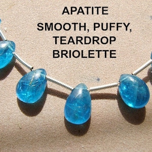 May include: A necklace made with smooth, puffy, teardrop briolette apatite beads. The beads are a vibrant blue color and are strung on a silver chain.
