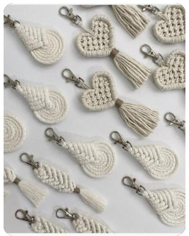 Puede incluir: Una colecci&oacute;n de llaveros de macram&eacute; en color blanco roto con dos dise&ntilde;os distintos: uno con forma de coraz&oacute;n con una borla colgante y otro con un patr&oacute;n trenzado en forma de hoja. Cada pieza est&aacute; unida a un mosquet&oacute;n de metal plateado.