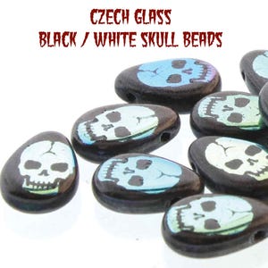 May include: A close-up of a group of black and white skull beads. The beads are made of Czech glass and have a iridescent finish. The beads are shaped like skulls and have a hole in the top for stringing.
