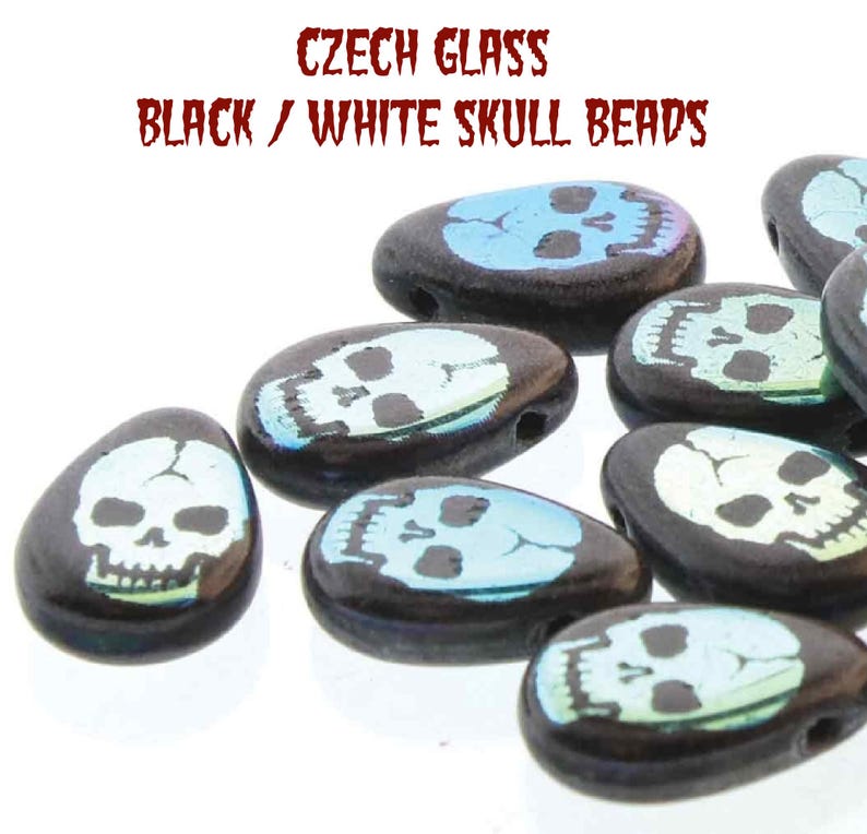 May include: A close-up of a group of black and white skull beads. The beads are made of Czech glass and have a iridescent finish. The beads are shaped like skulls and have a hole in the top for stringing.
