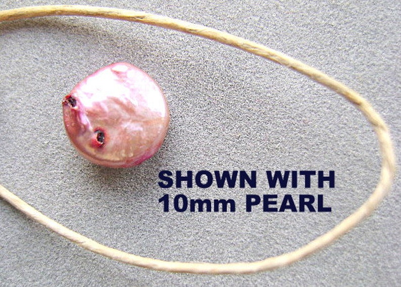 Puede incluir: Una perla redonda de color rosa iridiscente con hendiduras oscuras visibles en la superficie, colocada junto a un cord&oacute;n fino de color marr&oacute;n claro. El texto SHOWN WITH 10mm PEARL est&aacute; impreso en letras azul oscuro cerca de la perla.