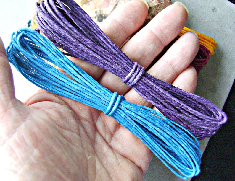 Puede incluir: Dos paquetes de cordel de m&uacute;ltiples hebras, uno en azul vibrante y otro en morado intenso. Cada paquete est&aacute; cuidadosamente enrollado y asegurado con un peque&ntilde;o lazo de cordel a juego. La textura del cordel parece fibrosa y mate, con un grosor constante.