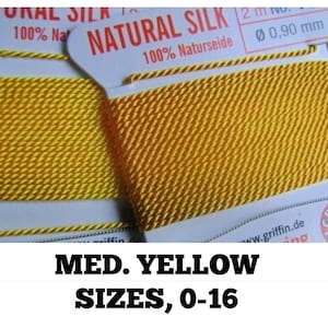Op de afbeelding: Twee spoelen gele natuurlijke zijde draad, gelabeld "NATURAL SILK 100% Naturseide" en "NATURAL SILK 100% Nat", met de tekst "MED. YELLOW SIZES, 0-16" eronder.