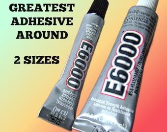 May include: Two silver tubes of E6000 industrial strength adhesive with black and white caps. The text E-6000 GREATEST ADHESIVE AROUND 2 SIZES is visible. The smaller tube is 0.18 fl oz and the larger tube is 0.5 fl oz. The tubes are silver.