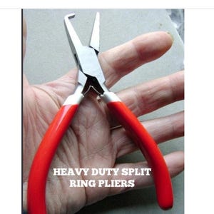 Op de afbeelding: Heavy-duty split ring tang met rode handgrepen en zilveren metalen bekken. De tang is ontworpen voor het openen en sluiten van splitringen. De tekst "HEAVY DUTY SPLIT RING PLIERS" is wit gedrukt.