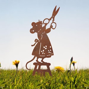 May include: A rust-colored metal silhouette of a mouse wearing an apron and standing on a small stool while holding a pair of open scissors above its head. The cutout design features detailed floral patterns on the apron and a long, thin tail.