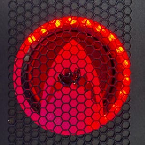 May include: Close-up of a computer fan with a red LED light. The fan is covered by a black honeycomb mesh. The fan's blades are visible through the mesh, and the red light illuminates the interior.