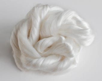 May include: A close-up of a large clump of white silk fibres. The fibres are soft and fluffy, and they are arranged in a loose, tangled mass.