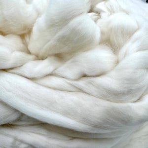 May include: Close-up of a pile of soft, white wool roving. The fibers are thick and fluffy, with a slightly textured appearance. The wool is tightly packed in a swirling pattern, creating a sense of depth and volume. Ideal for fiber art projects.