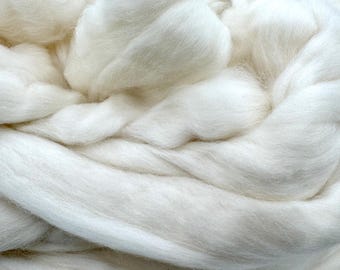 Könnte beinhalten: Nahaufnahme eines Haufens weicher, weißer Wollrovinge. Die Fasern sind dick und flauschig, mit einem leicht strukturierten Aussehen. Die Wolle ist dicht in einem Wirbelmuster gepackt, wodurch ein Gefühl von Tiefe und Volumen entsteht. Ideal für Bastelprojekte.