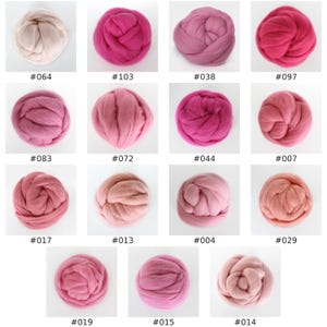 May include: A collection of fifteen round bundles of roving wool in various shades of pink, ranging from pale blush and peach to deep magenta and mauve. Each bundle is labeled with a specific number from #064 to #014, arranged in a grid.