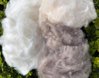 May include: Two piles of natural fiber, one white and one light brown, against a green leafy background.