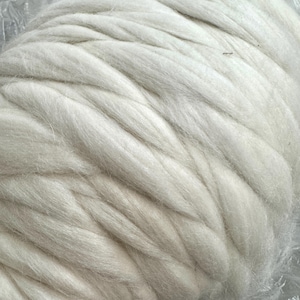 May include: Close-up of a large, off-white roving yarn bundle. The fibers are thick and loosely spun, with a soft, textured appearance. The yarn is tightly wound, creating a dense, yet pliable form, ideal for various fiber art projects.