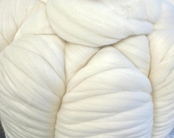 May include: A large, white, fluffy pumpkin-shaped creation made of thick wool roving. A small, orange pumpkin with a green stem sits on top. The wool is tightly packed and appears soft.