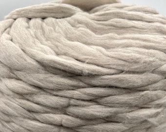 May include: Close-up of a large, light gray ball of super chunky merino wool yarn. The thick strands are tightly wound, creating a textured surface. Ideal for arm knitting or creating large, cozy projects.