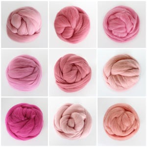 Puede incluir: Nueve ovillos de lana en varios tonos de rosa y melocotón. La lana está dispuesta en tres filas de tres ovillos cada una.