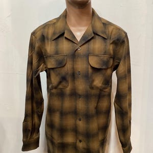 以下が含まれることがあります： 茶色と黒のチェック柄の長袖ボタンダウンシャツ。 シャツにはフロントポケットが2つとクラシックな襟が付いています。 生地は柔らかく織られた素材のようです。 シャツはマネキンに表示されています。