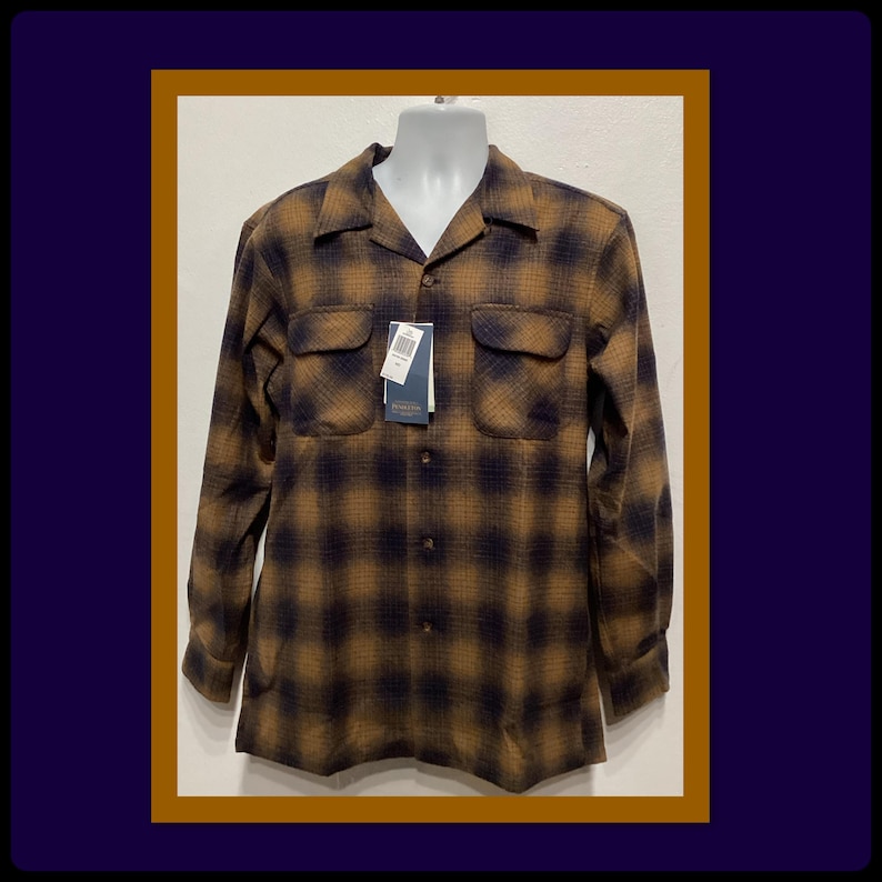 Puede incluir: Una camisa de manga larga de cuadros marrones y negros con cuello y cierre de botones. La camisa tiene dos bolsillos en el pecho y una etiqueta que dice "Made in USA".