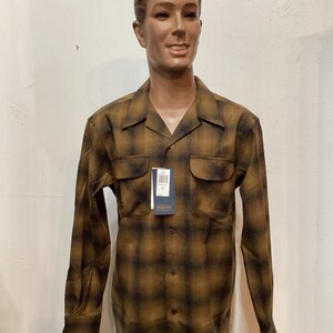 以下が含まれることがあります： 茶色と黒のチェック柄長袖シャツ。胸ポケットが2つと襟が付いています。マネキンに着せられています。シャツにはタグが付いています。シャツは柔らかく快適な素材で作られています。