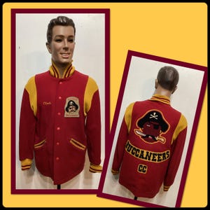 May include: A vintage red and yellow letterman jacket with the word "Coach" embroidered on the front. The jacket features a pirate logo and the word "Buccaneers" on the back. The jacket is displayed on a mannequin.