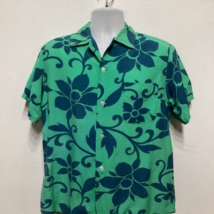 May include: A short-sleeved button-down shirt in a vibrant green hue, adorned with a bold floral pattern in a contrasting dark teal. The shirt features a classic collar, a chest pocket, and white buttons.