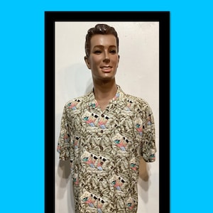 May include: A short-sleeved button-down shirt featuring a repeating pattern of brown tropical leaves and small diamond-shaped inserts containing illustrations of sailboats on blue water with red and white accents, worn by a male mannequin.