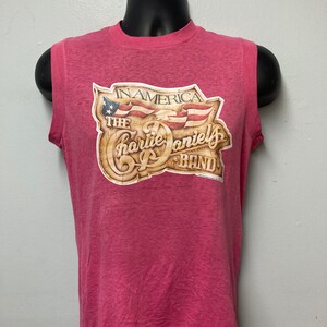 May include: A pink sleeveless t-shirt with a vintage graphic print of "The Charlie Daniels Band" with the text "In America" and a stylized American flag.