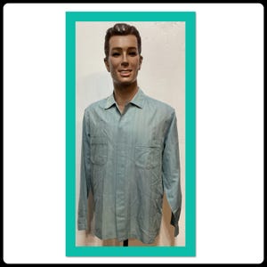 Puede incluir: Una camisa de manga larga azul claro con un sutil patrón a rayas. La camisa tiene cuello y dos bolsillos en el pecho.