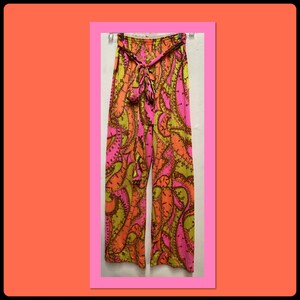 May include: Wide-leg pants with a vibrant paisley pattern in shades of pink, orange, and yellow. The pants have a matching fabric belt that ties at the waist. The pants are hanging against a white background.