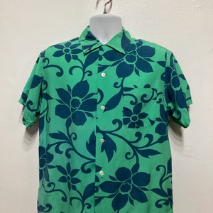 May include: A short-sleeved button-down shirt in a vibrant green hue, adorned with a bold floral pattern in a contrasting deep teal. The shirt features a classic collar, a chest pocket, and white buttons.