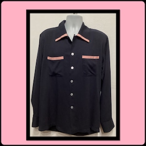 May include: A black long-sleeve shirt with a camp collar and two chest pockets. The collar and pocket trim are a light peach color. The shirt has a button-down front with white buttons.