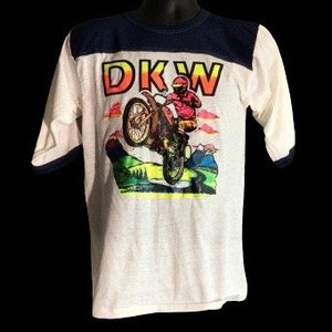 May include: White t-shirt with a blue and white striped collar and sleeves. The front of the shirt features a graphic of a person riding a dirt bike with the text "DKW" in rainbow colors.