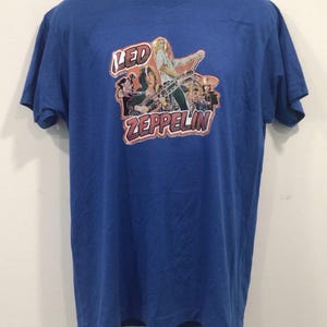 May include: A blue t-shirt with a vintage Led Zeppelin graphic print featuring a photo of the band members. The print includes the band's name in a stylised font.