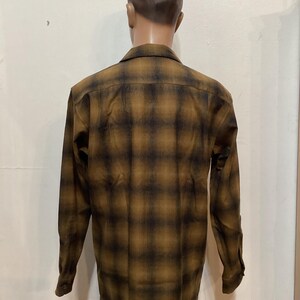 以下が含まれることがあります： 茶色と黒のチェック柄の長袖ボタンダウンシャツ。マネキンに着せられており、背中から見た様子。生地は中程度の厚さに見えます。肌寒い季節に適しています。