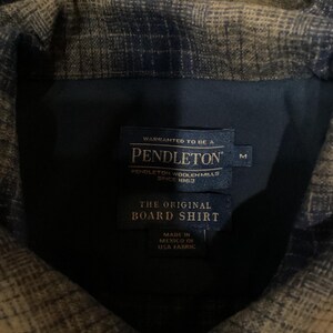 Puede incluir: Una camisa Pendleton de cuadros marrones y azules con una etiqueta que dice "WARRANTED TO BE A PENDLETON PENDLETON WOOLEN MILLS SINCE 1963 THE ORIGINAL BOARD SHIRT MADE IN MEXICO OF USA FABRIC" y una etiqueta de talla que dice "M".