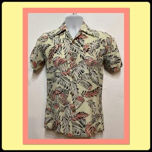 Op de afbeelding: Korte mouwen button-down shirt met een crèmekleurige achtergrond en een tropische print. De print toont roze en bruine drums, palmbladeren en andere tropische elementen. Het shirt wordt op een mannequin getoond.