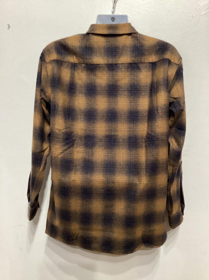 Puede incluir: Una camisa de manga larga con botones y un estampado de cuadros marrones y negros.