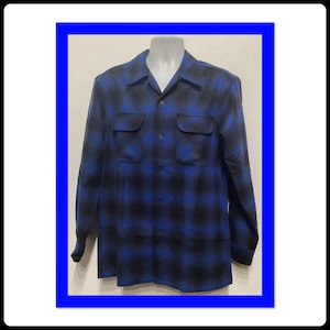 Könnte beinhalten: Ein langärmliges Hemd mit Knöpfen und einem blau-schwarzen Karomuster. Das Hemd hat einen Kragen und zwei Pattentaschen auf der Brust.