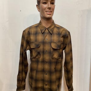 以下が含まれることがあります： 茶色と黒のチェック柄のボタンダウンシャツ。胸ポケットが2つ付いています。長袖シャツはマネキンに着せられています。シャツはクラシックな襟とボタン留めです。